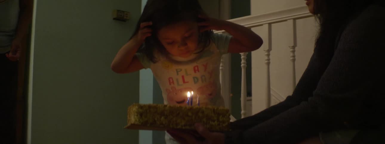 A toddler smiles and cheers after blowing out candles on her birthday cake