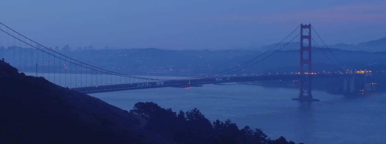 Aerial shot of a bridge over water at night with traffic and car lights in distance