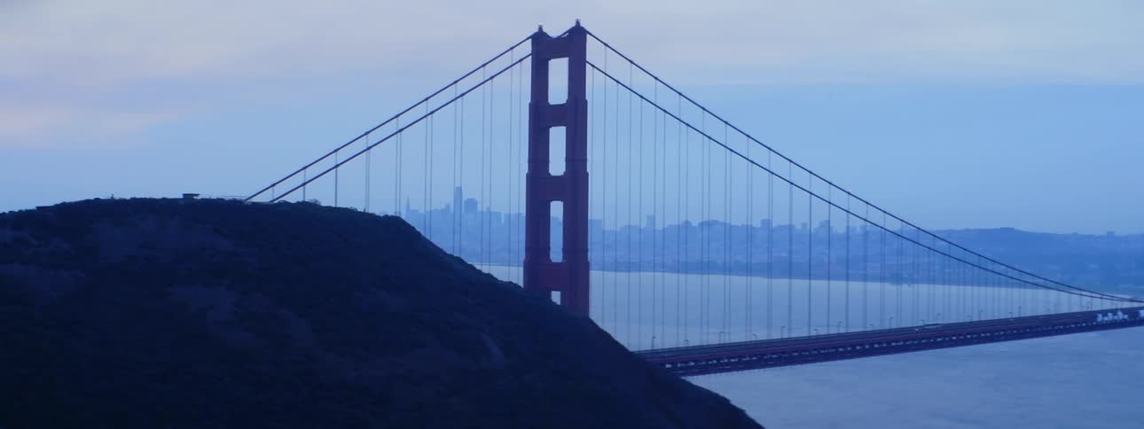 Mist obscures the city as vehicle crosses suspension bridge near promontory