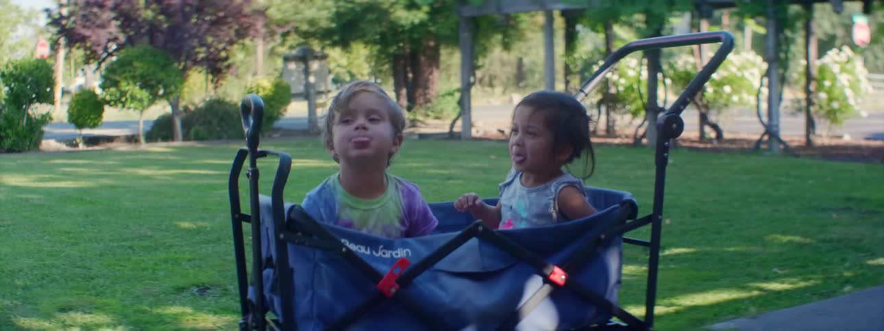 Two kids sitting in baby cart on path in park play and make faces