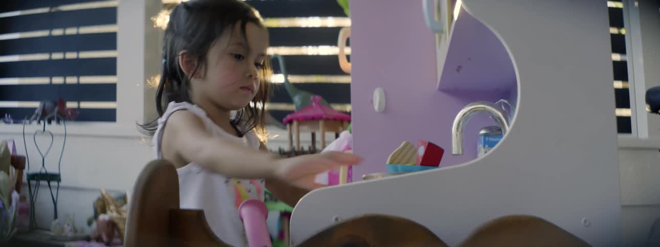 A girl is washing dishes in her play kitchen