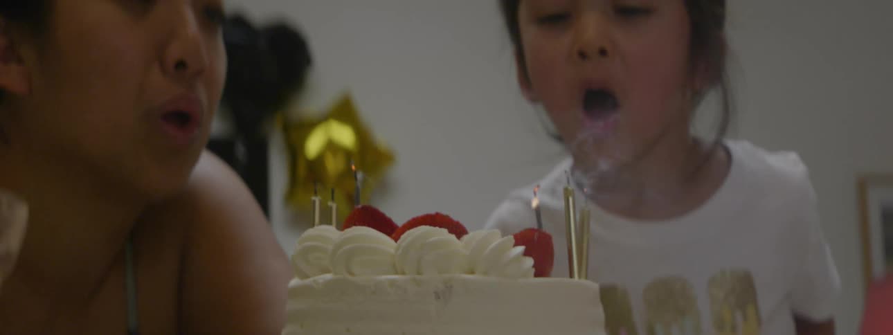 Mother and daughter sitting at a table blowing out candles on a birthday cake