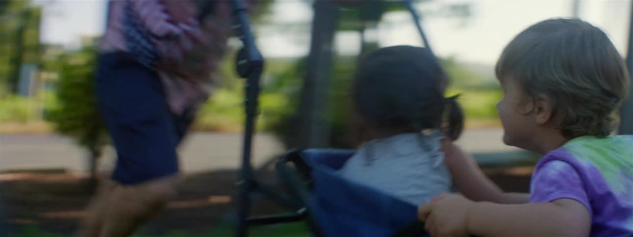 A woman twirls her children around in a wagon at a park