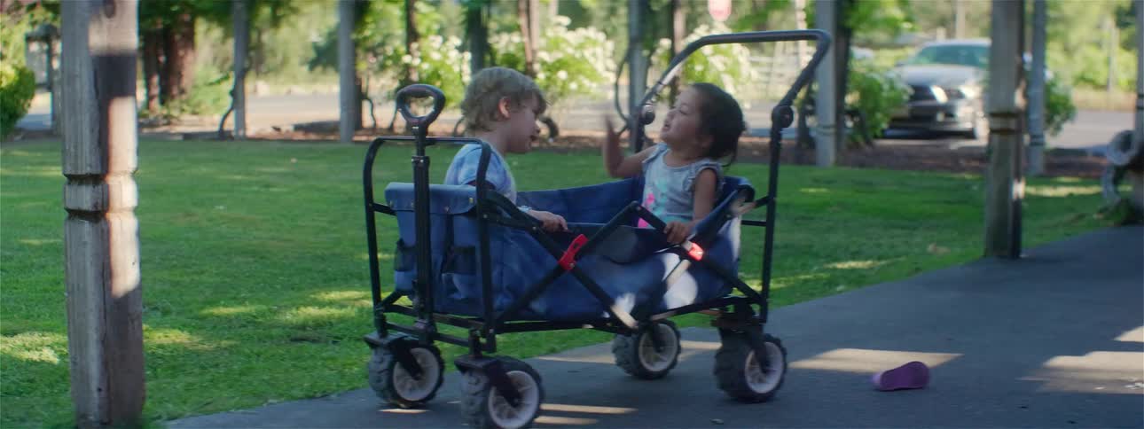 Two toddlers sitting in a stroller outside at daytime playing around and throwing their shoes