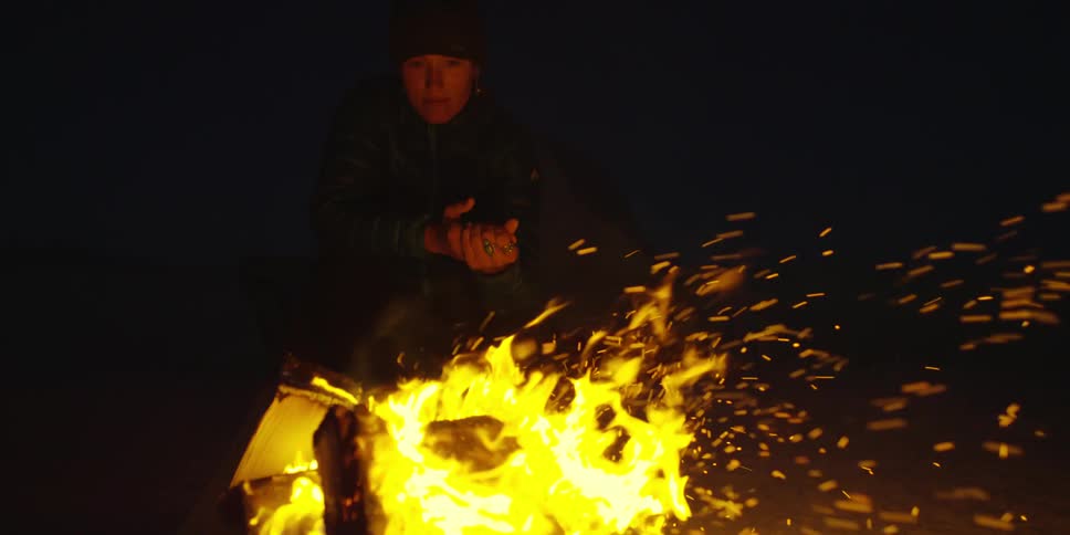 A woman warming her hands with a campfire