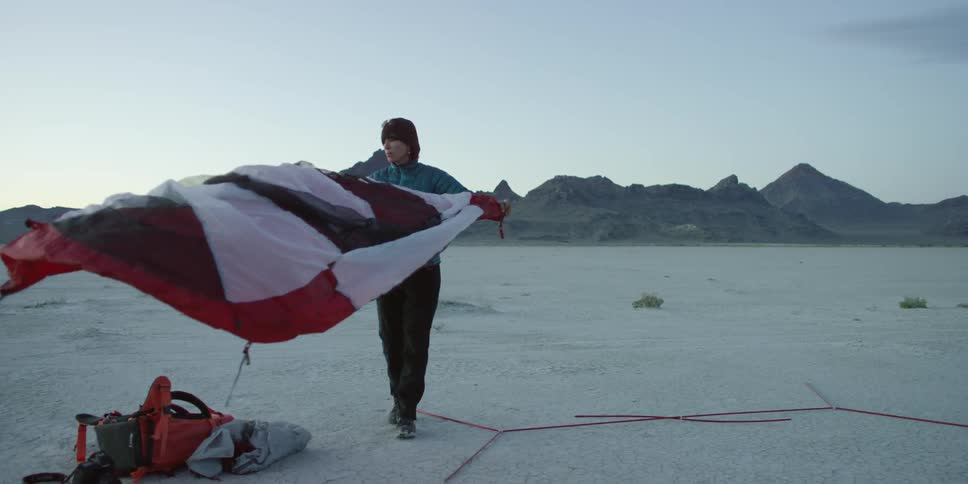 A woman shaking a tent out and laying it on the ground