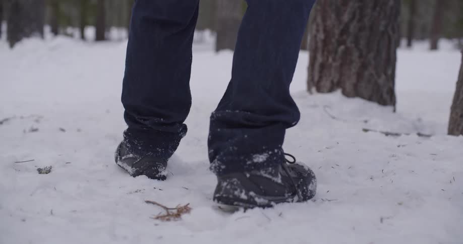 Pair of feet walking in a snow covered ground in a forest at day time