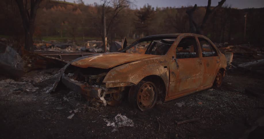 Rusted old car missing tires and windows sitting in a junkyard outdoors at sun set