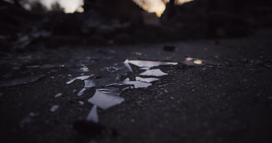 Broken glass lays on road with the orange of sunset reflecting off it