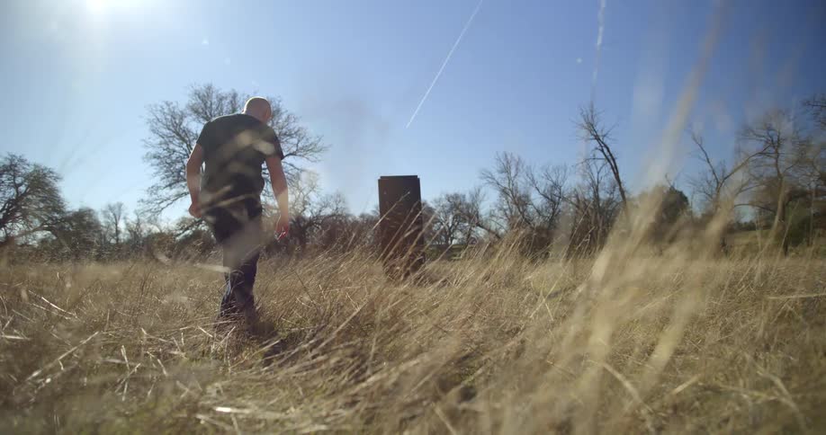 A man walks towards an object in a grassy field in daylight