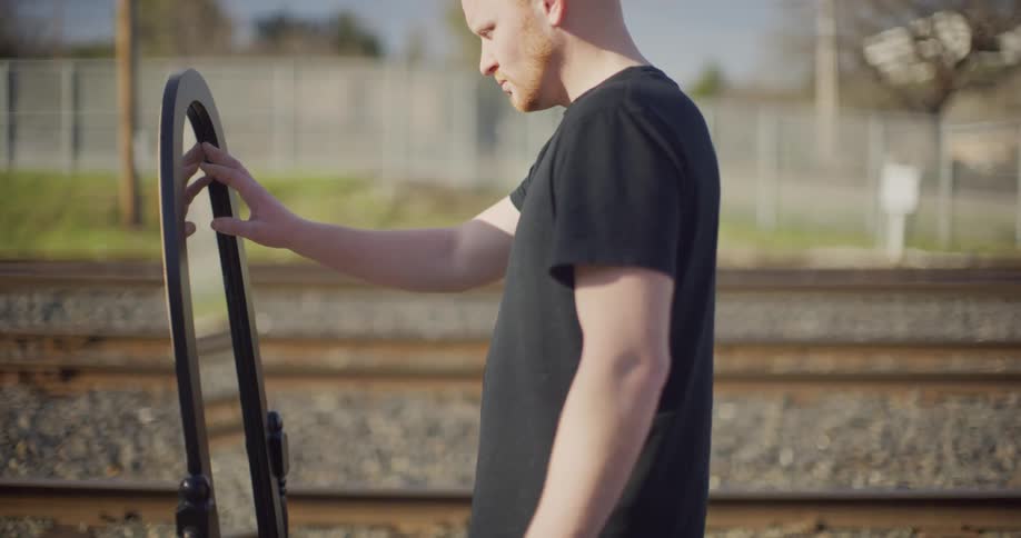 A man looks at a mirror and grazes it with his fingertips