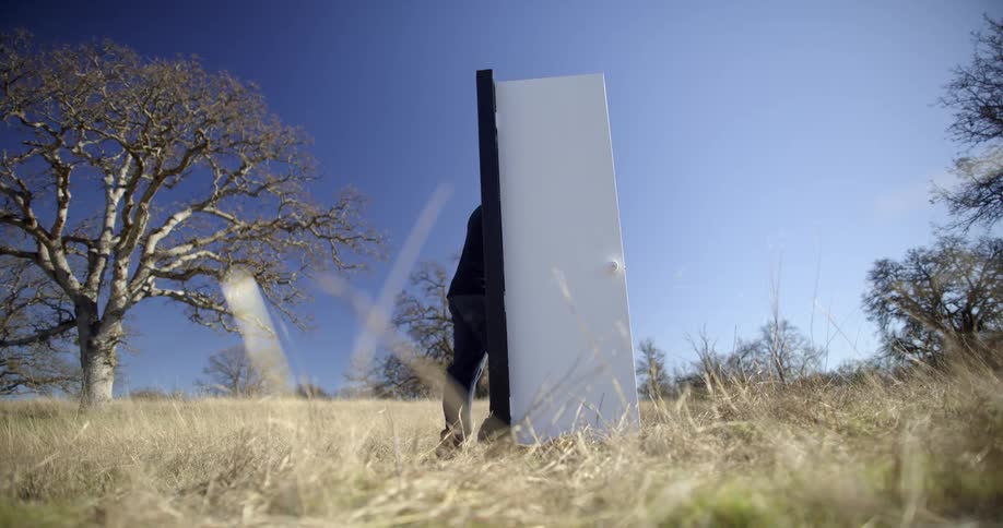 Man opens and walks through free standing door in middle of field