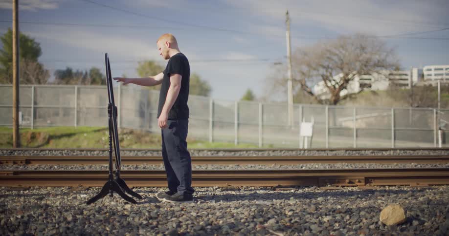 A man stands outside on a gravel ground reaching to touch a sign