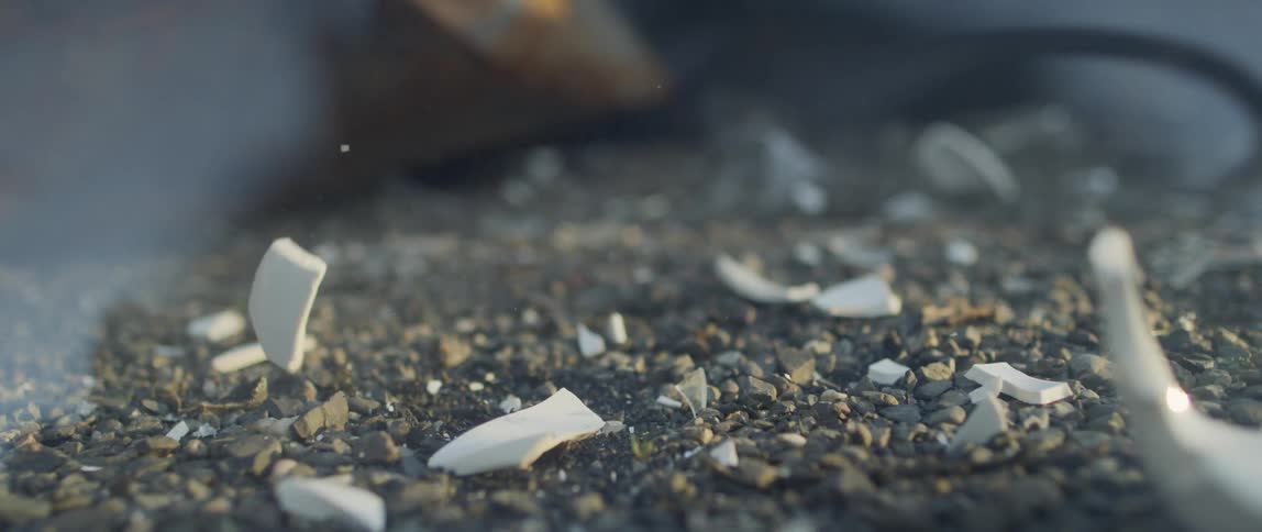 A porcelain coffee mug on the ground is smashed to pieces with a stick