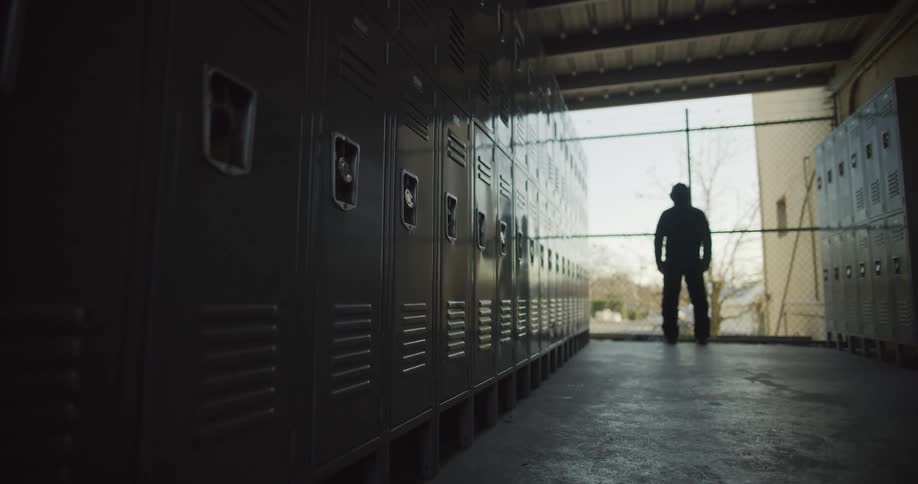 A man stands at the end of a row of lockers in a locker room looking out of a window floor to ceiling window
