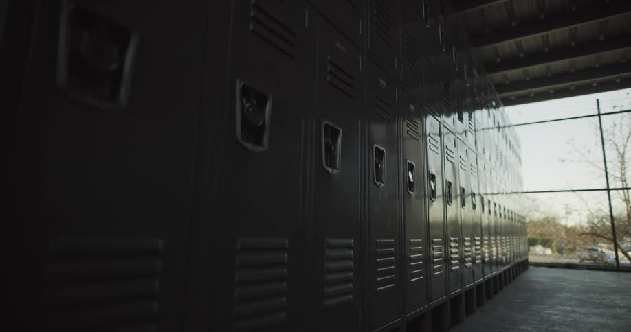 Lockers in a school hallway some in shadow some in light in front of a window where you can see cars and trees