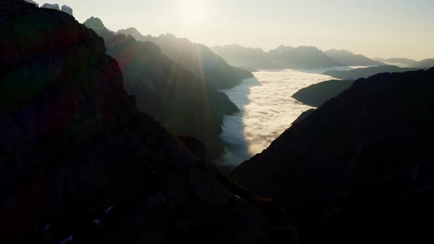 Sun shining above mountain peaks with snow in between them
