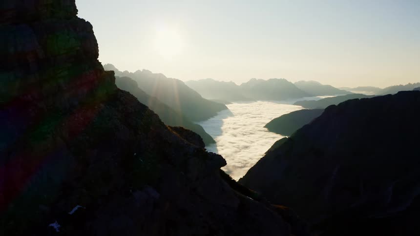 A valley tucked within a range of mountains is filled with clouds