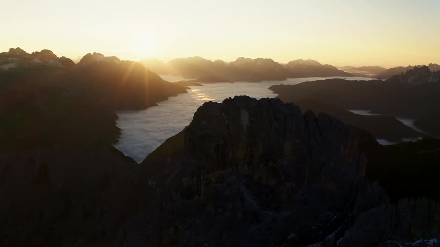 Sun rising over a set of mountains peaks with a small valley covered in clouds