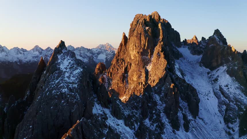 A mountain range with snow with the sun low in the sky