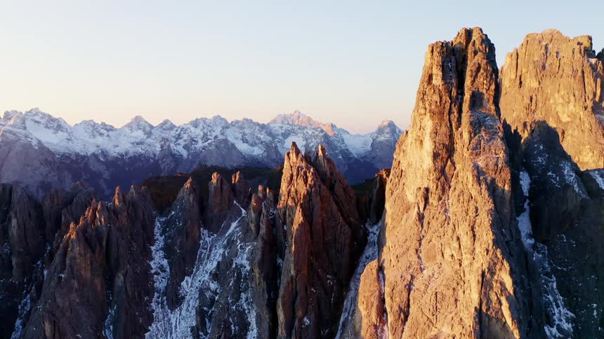 Sun shines on jagged rocky mountain ridges and peaks dotted with snow and ice