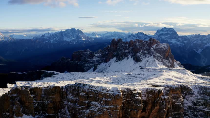 An aerial view of a mountain range with snow and clouds in the sky