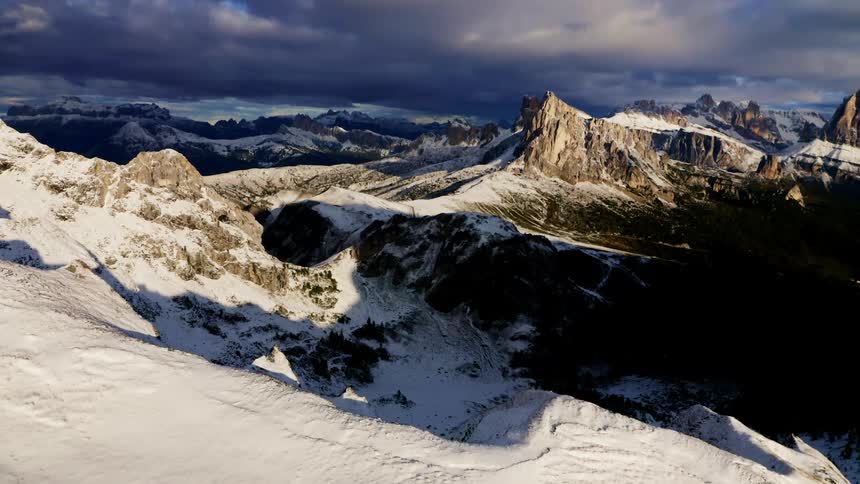 A mountain range covered in snow under dark storm clouds
