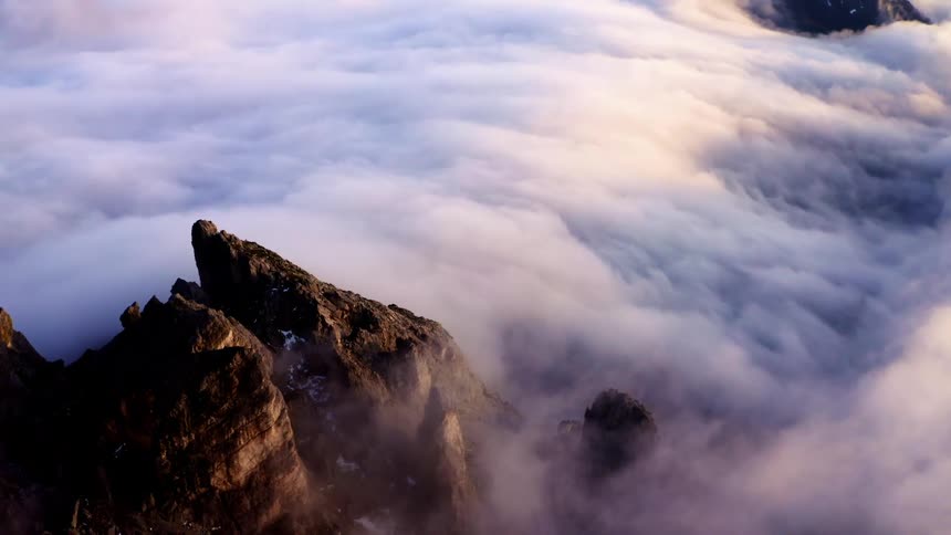 Snow dotted craggy mountain peaks peak over heavy clouds