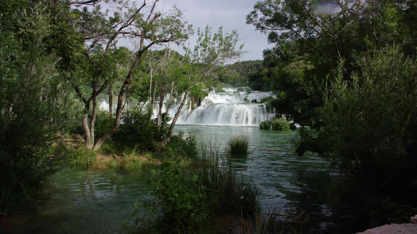 Small waterfall in a river flowing between the trees and bushes in the hills