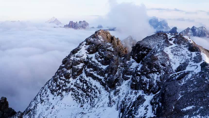 A snow capped mountain peak looms over the sea of clouds obscuring the landscape below