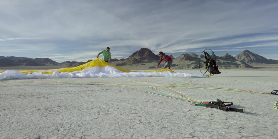 Two people adjust a parachute that is spread out on the ground