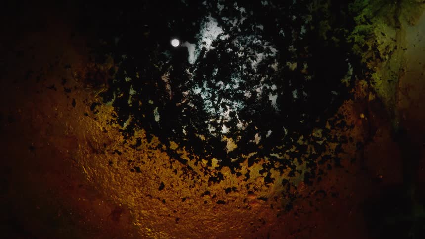 Bronze and black liquids moving outwards and swirling into each other