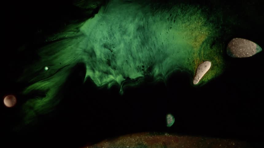 A green fluid with an unusual texture flows across a darkened surface