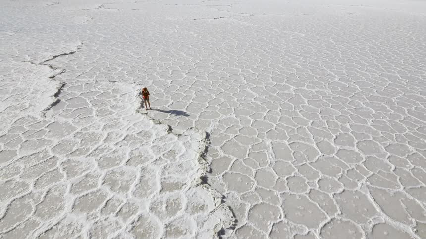 A person walks across the cracked ground of the desert
