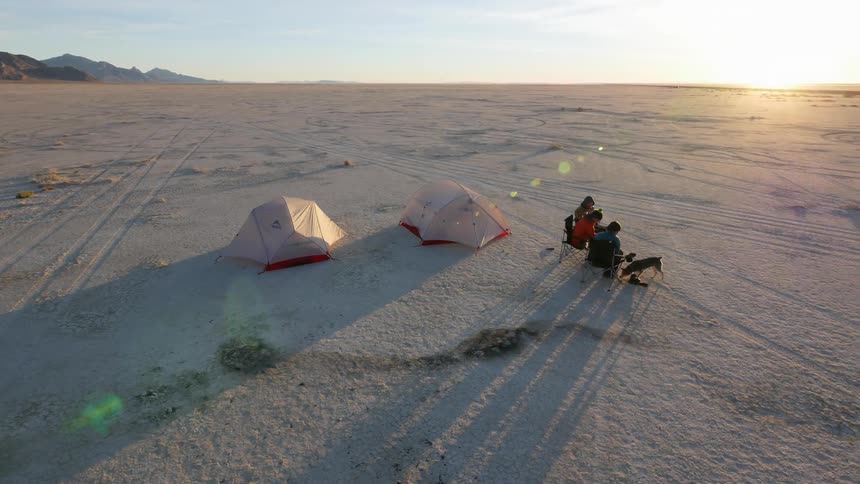 People are playing with a dog near two tents on a large desert
