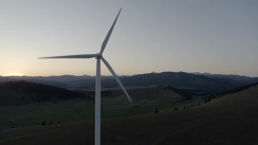 Orbiting around a single wind turbine with the sun setting behind mountains in the distance