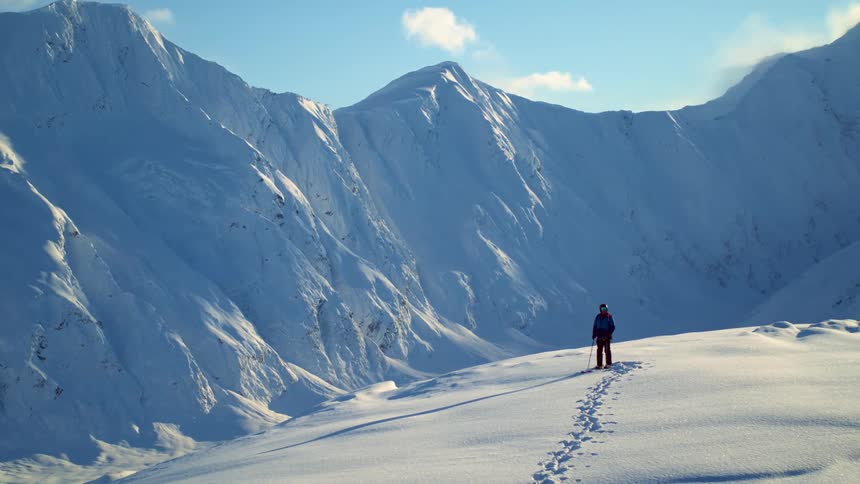 A person trekking through snow and standing on a mountain