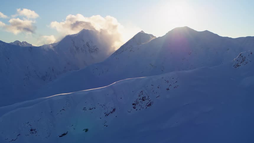 Snowy mountain peaks with slopes and clouds above them on a sunny day