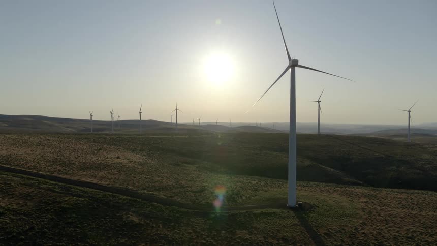 Low angle traverse around a motionless wind turbine on a completely idle wind farm at sunrise