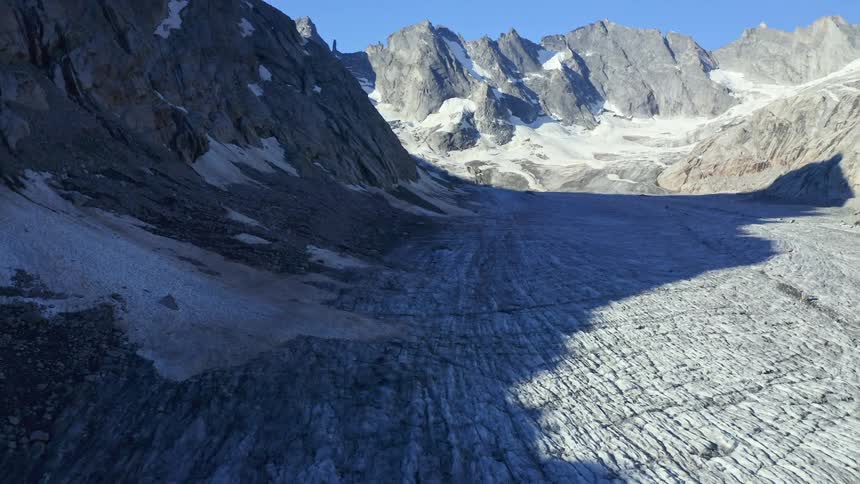 Rock formations on top of a snowy mountain at day time next to a small cliff casting shadows on a slope