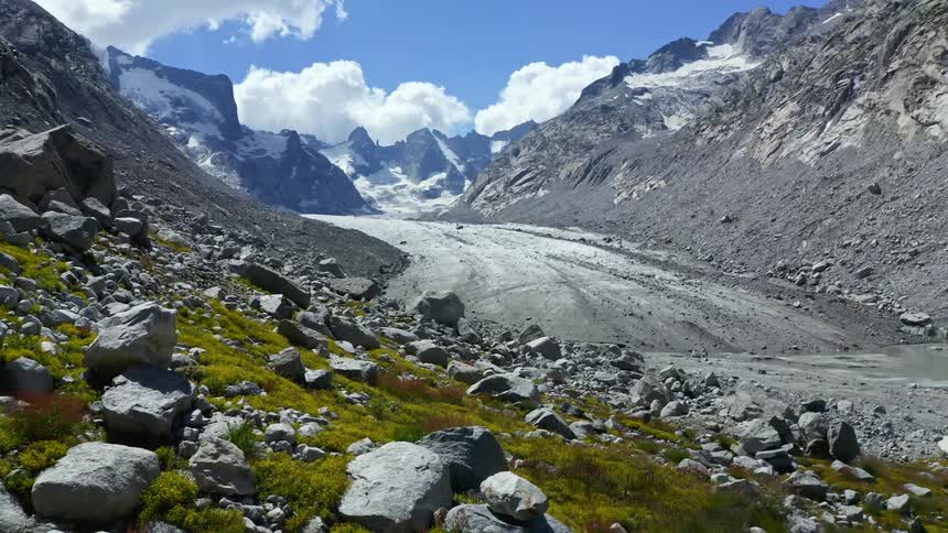 Mossy vegetation and rocks cover slope near road leading to snow covered mountains