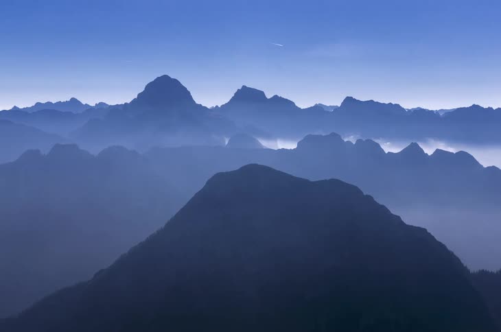 Fog flows across the peaks of a mountain range on a sunny day