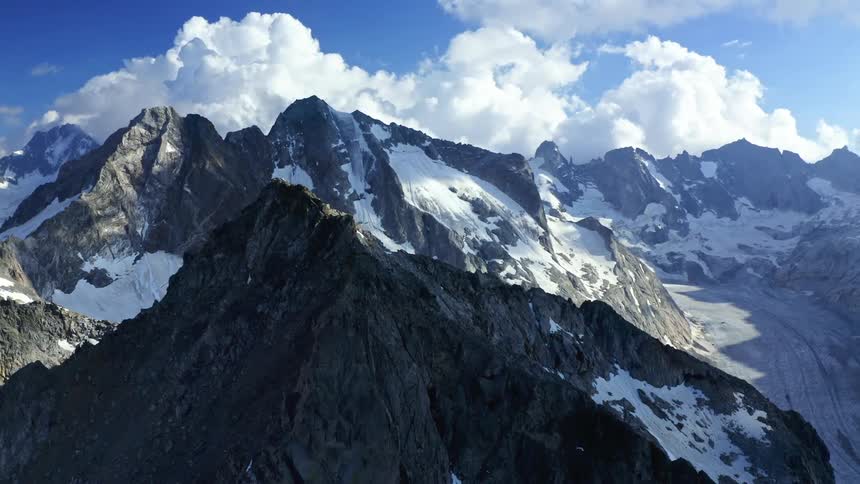 Aerial view of snowy rugged mountains against the blue sky with white clouds