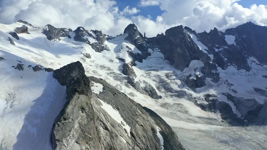 Snow capped rugged mountains against the blue sky with white clouds