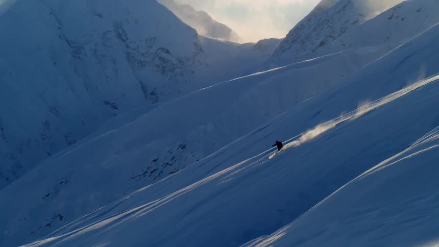 Man skiing down a snowy mountain slope at daytime