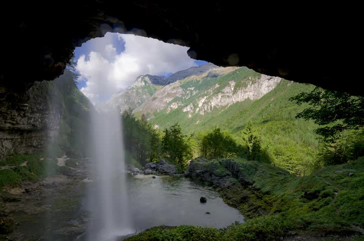 Water falls into a small body of water near a mountain range
