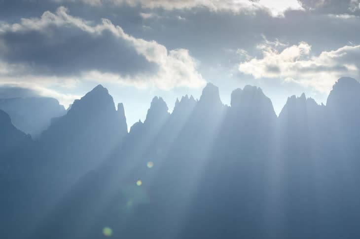 Mountains with fast moving clouds against a blue sky with sun rays