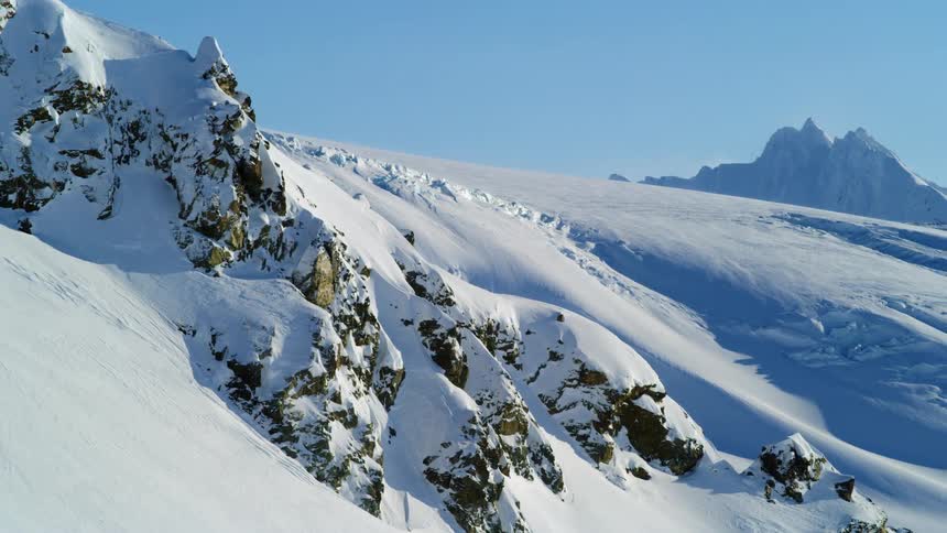 Snow covers the slope of a rocky mountain range under clear skies