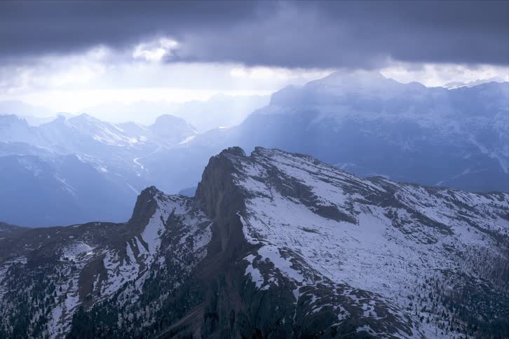 Beams of sunlight peak through heavy clouds that move over a mountain range