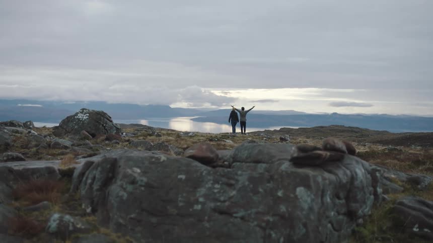 Two people are on the top of a mountain with one outstretching his arms to the sky